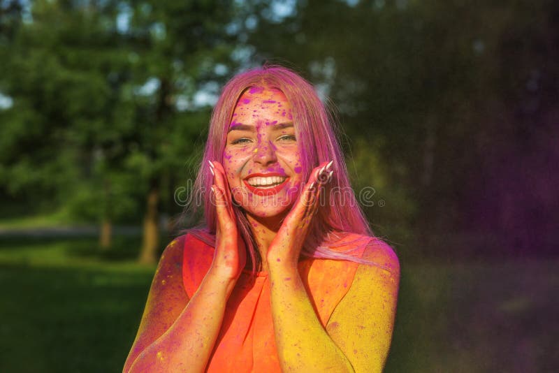 Attractive blonde woman having fun with colorful dry paint at the park. Concept for festival Holi. Attractive blonde girl having fun with colorful dry paint at stock photos